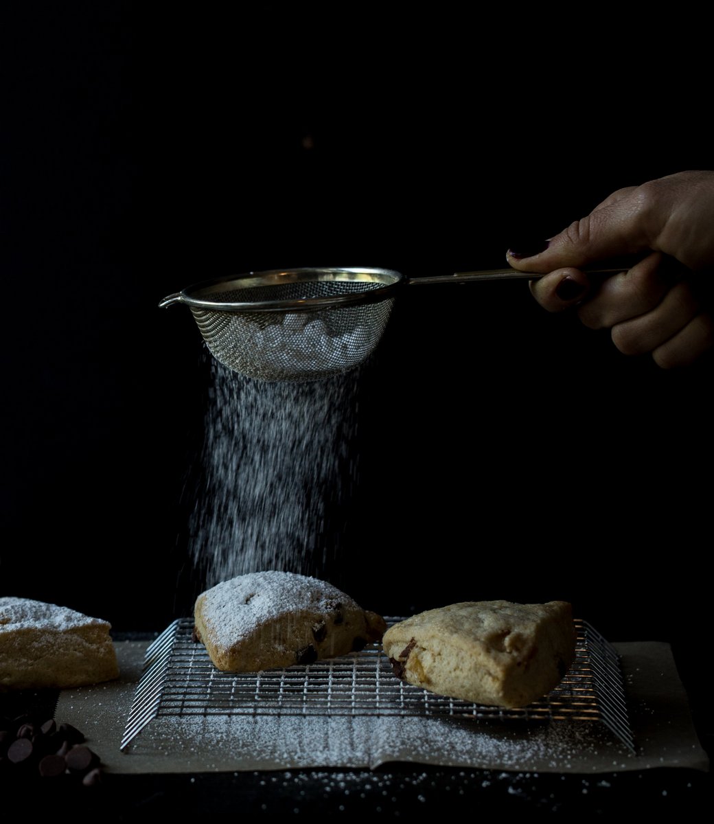 Woman sprinkling powdered sugar over scones in dark and moody food photo