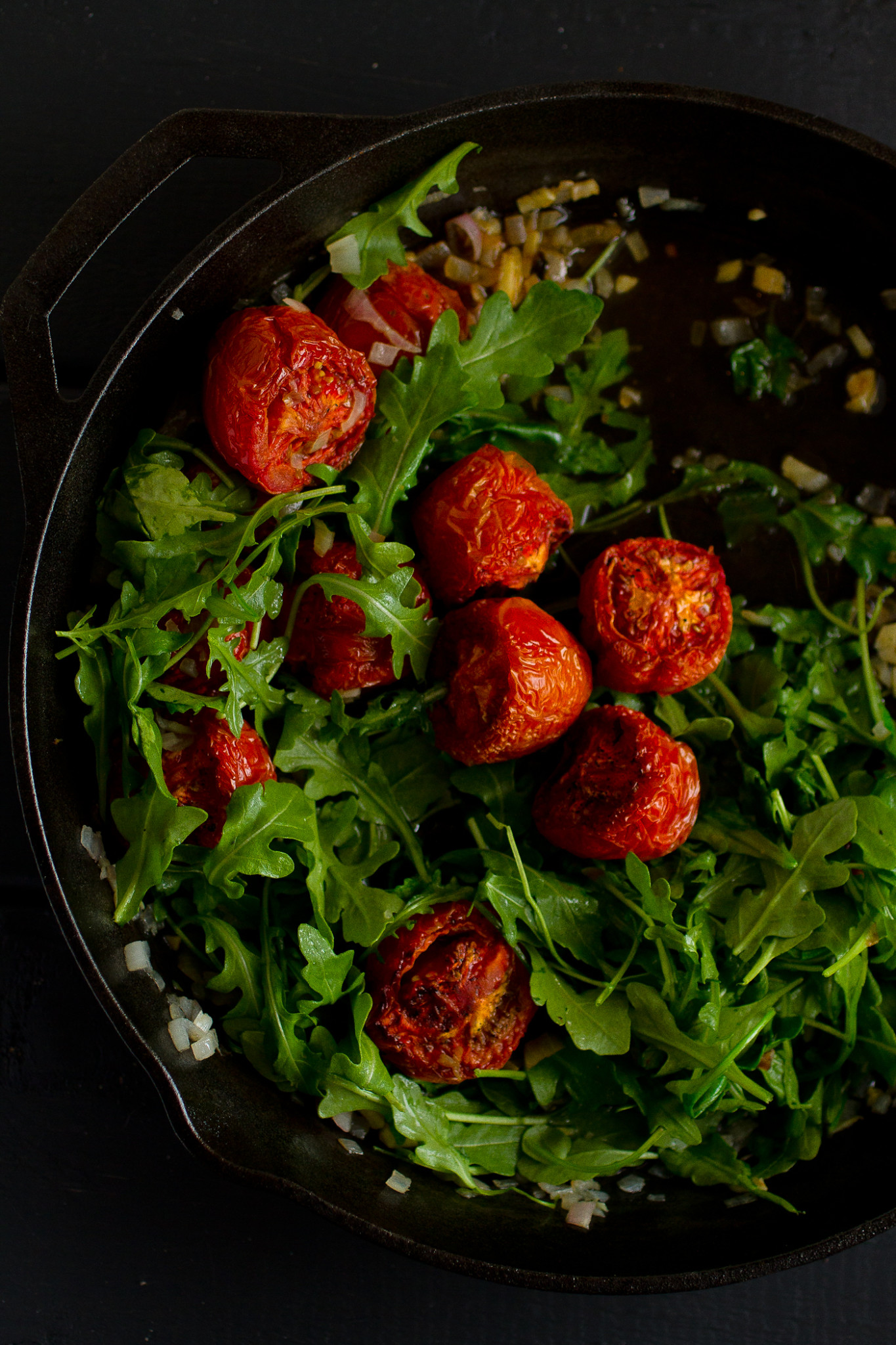 Cast iron skillet with roasted cherry tomatoes and arugula food photo