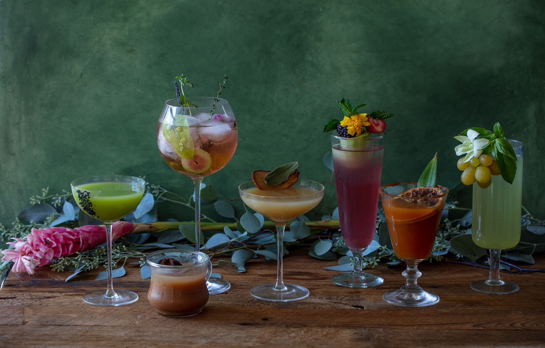 Seven harvest cocktails on wooden table with fresh fruit garnishes