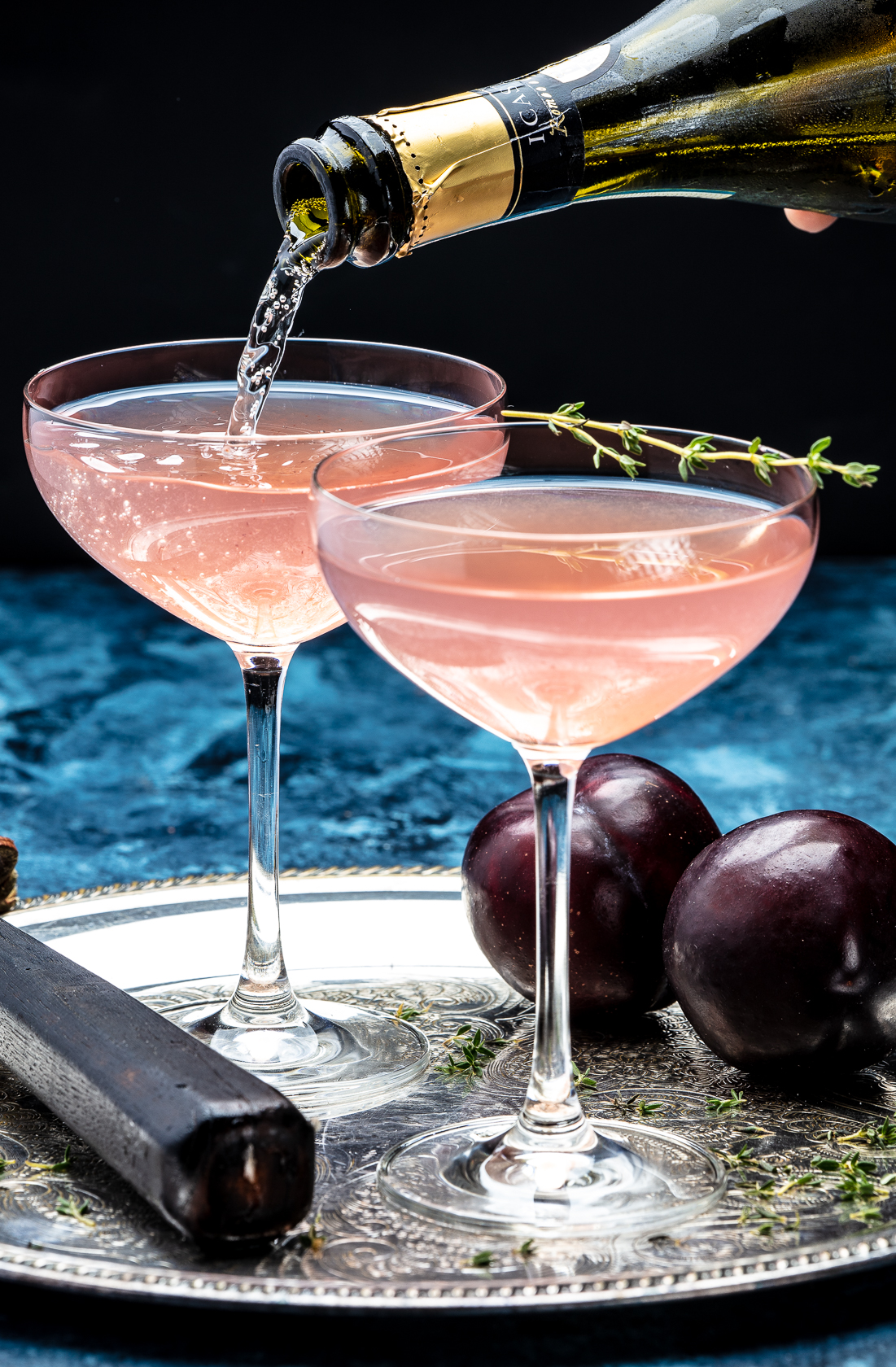 Champagne poured into holiday cocktails with rosemary and plums