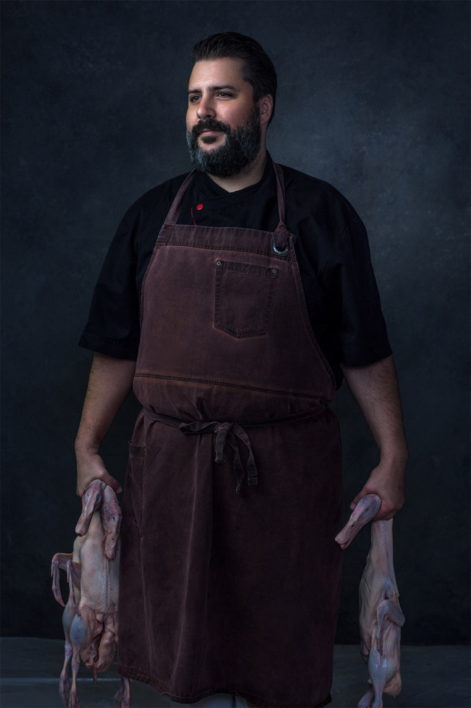 Beautiful moody portrait of chef in butcher apron holding three dead geese