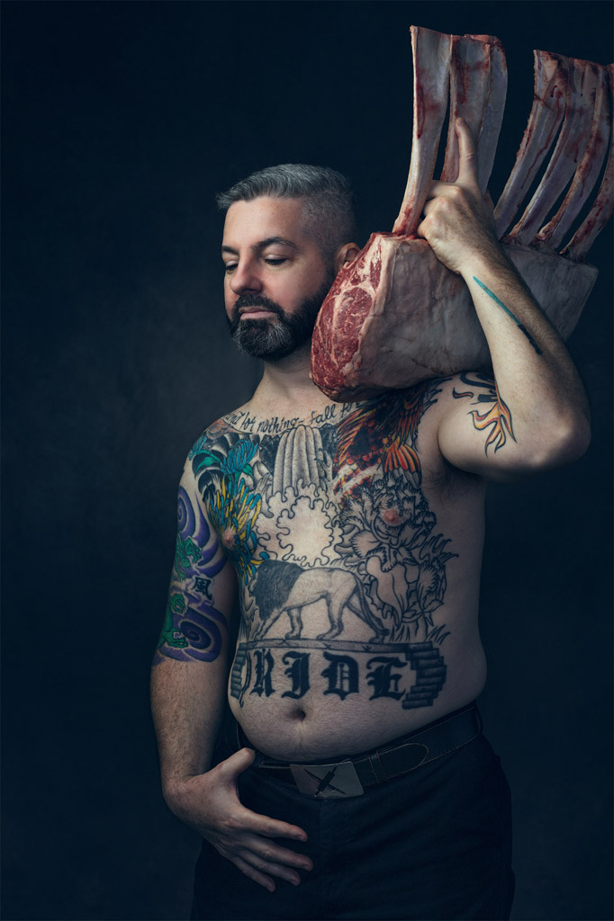 Half naked chef covered in tattoos holding large side of ribs