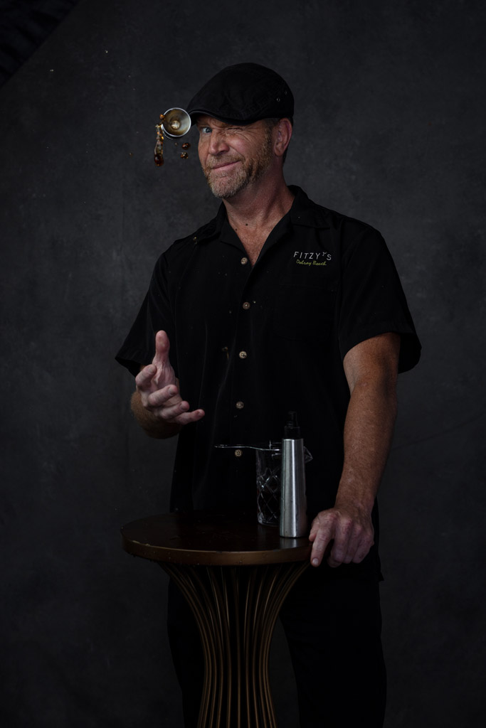 Fun photo of bartender winking as he tosses a jigger of whiskey in the air