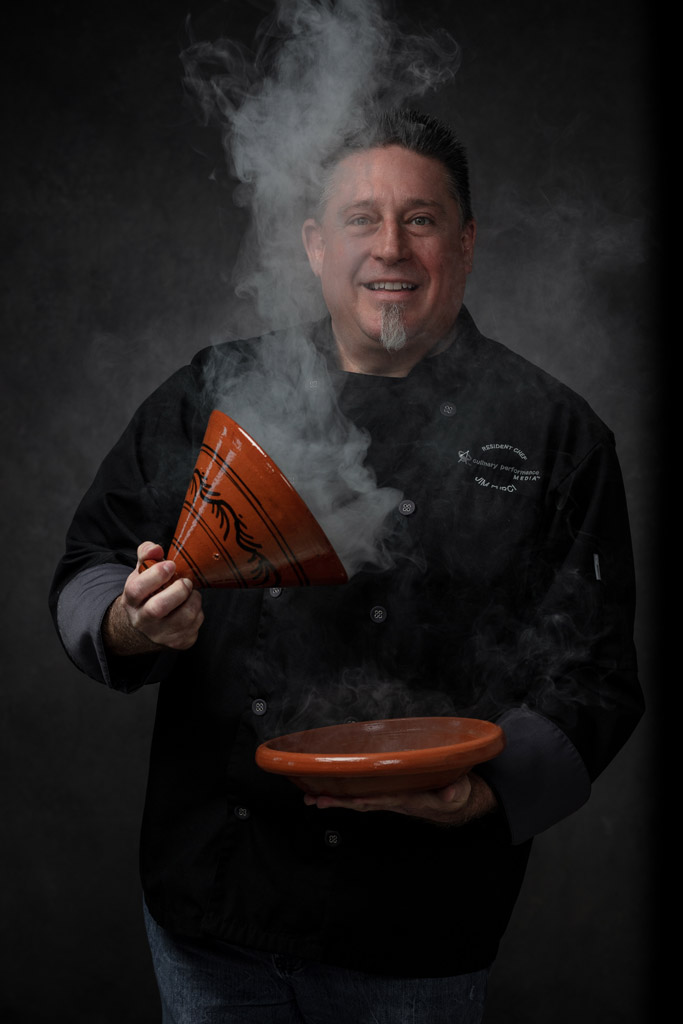 Compelling moody photo of chef holding Tagine and smoke covering his face