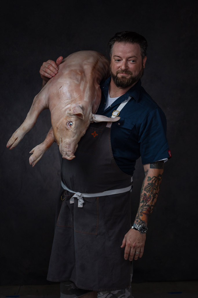 Hot chef covered in tattoos holding pig over his shoulder