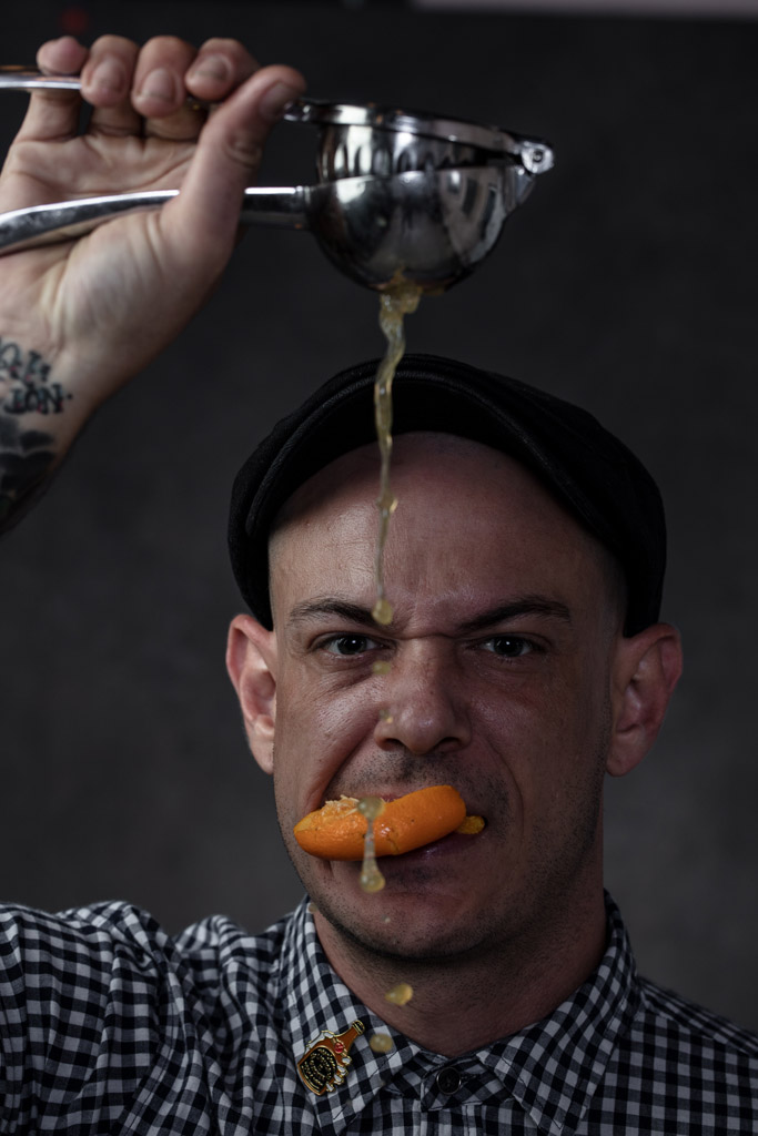Intense portrait of mixologist squeezing citrus with an orange in his mouth