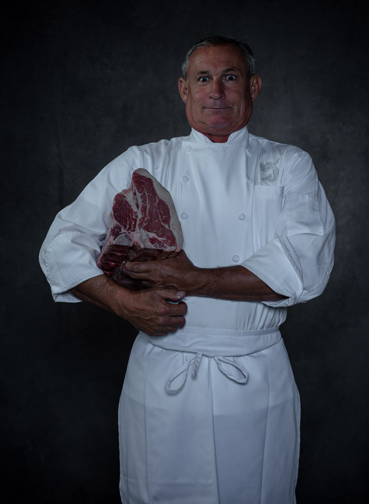 Happy and intense photo of Italian chef with large cut of meat under his arm and grinning at the camera