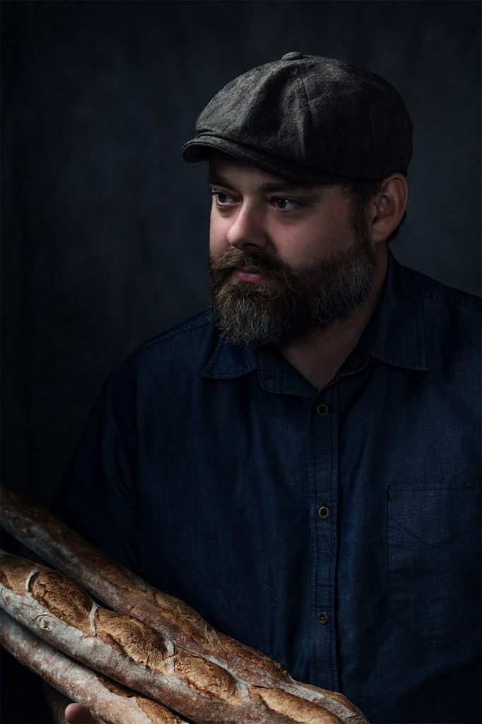 Creative portrait of baker in hat holding baguettes in beautiful lighting