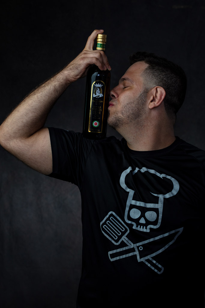 Attractive chef and olive oil importer kisses a bottle of olive oil balanced on his large bicep