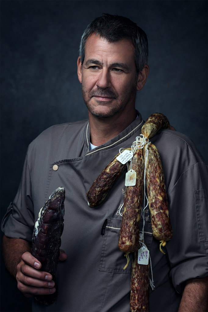 Chef holds salami and dried meat in moody photo