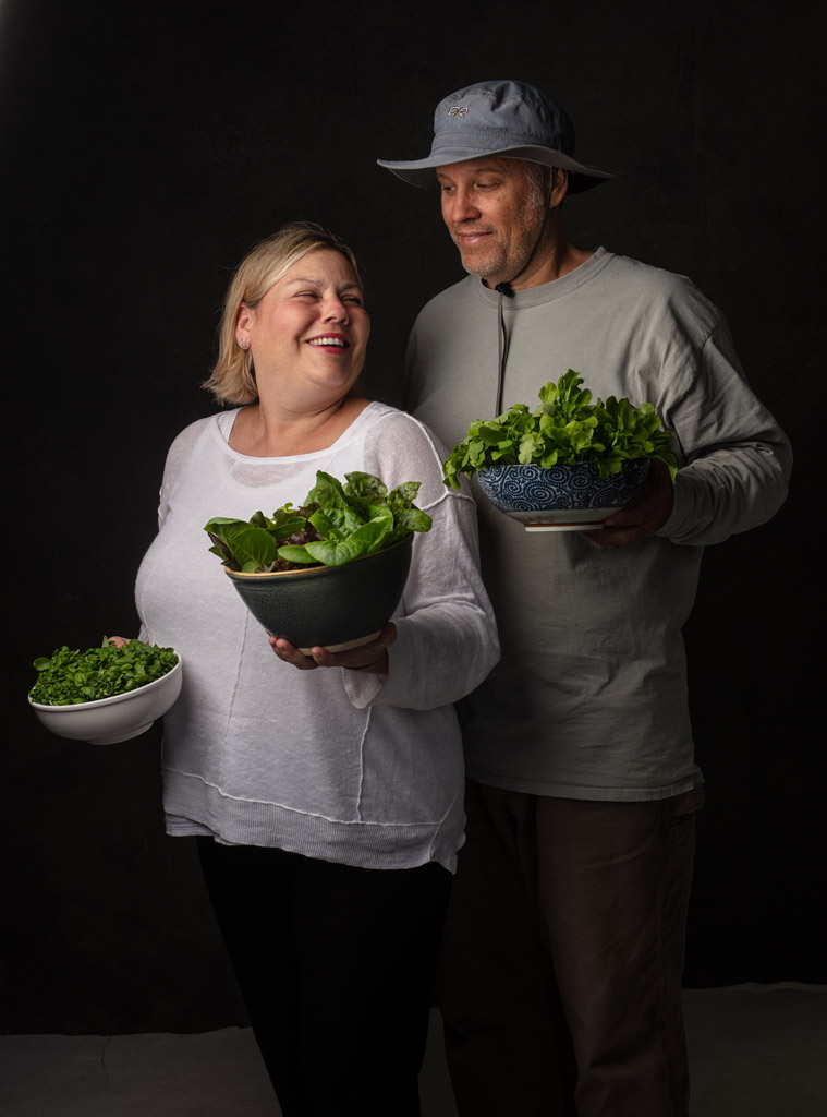 Farmers smile at each other while holding bowls of fresh greens