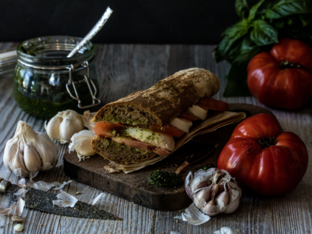 Tomato pesto and mozzarella panini on a wood cutting board with tomatoes and garlic