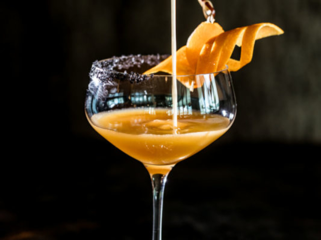 Orange cocktail being poured into fancy coup glass with exotic garnish