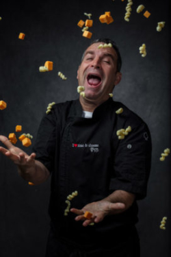 Chef smiling with his mouth open as raw macaroni and chunks of cheese fall from the heaven