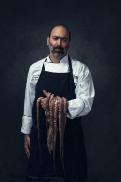 Stunning, creative portrait of chef holding octopus over his arm