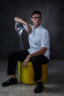 Attractive chef with extra large spoon sitting on yellow stool
