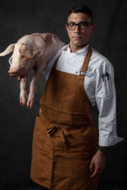 Moody photo of chef with whole pig over his shoulder in butcher apron