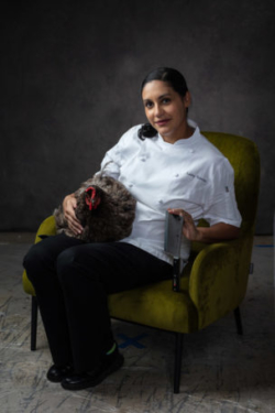 Chef holding a rooster and a knife smiling at camera.