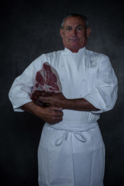 Happy and intense photo of Italian chef with large cut of meat under his arm and grinning at the camera