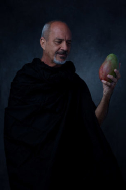 Moody and intense portrait of famous chef holding a mango and studying it while draped in black cloth