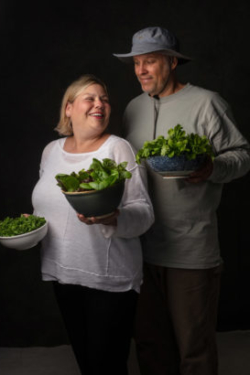 Farmers smile at each other while holding bowls of fresh greens